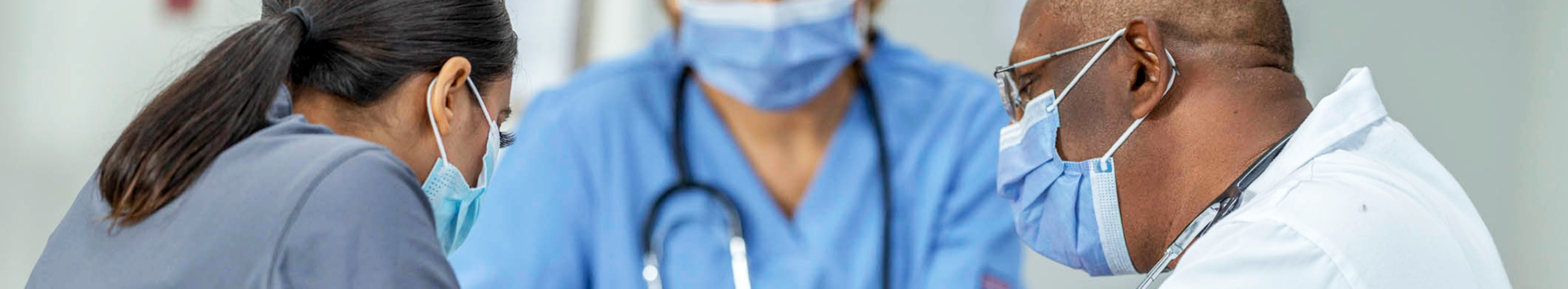 A group of health care workers sit together at a table and discuss information on a clipboard. 