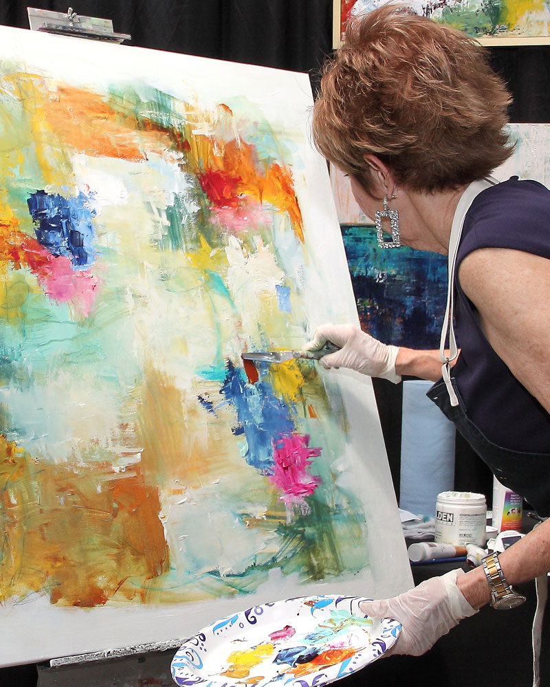 An artist works on a colorful abstract canvas at the ArtBlink event.