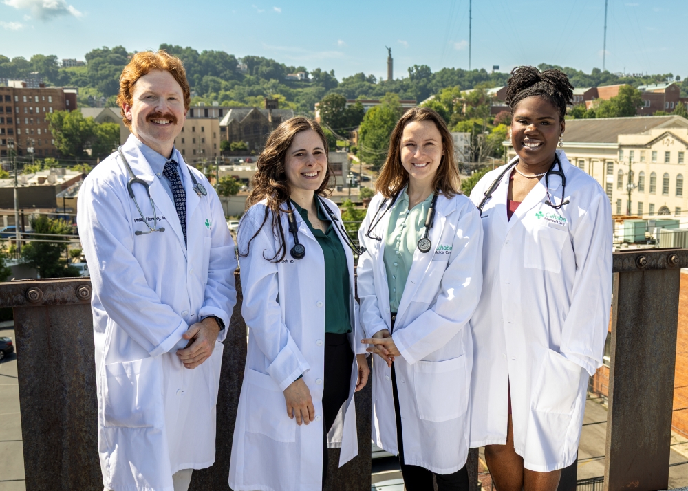 Four people in medical white coats stand in front of Birmingham skyline