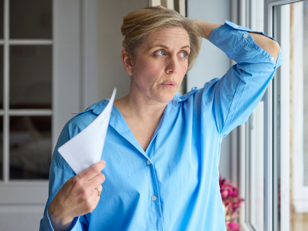 Woman fans herself with paper while looking out window