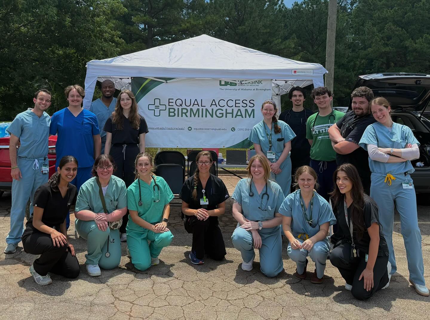 Group of medical students in scrubs posing for a photo in front of an Equal Access Birmingham tent