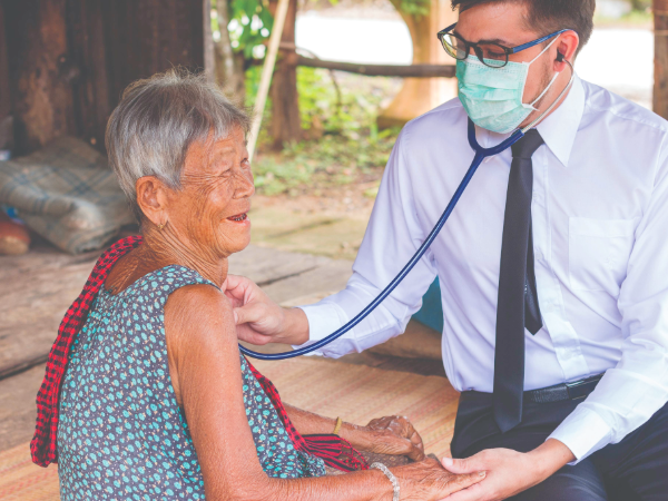 Masked clinician checks an older patient’s heart with a stethoscope during a community health visit