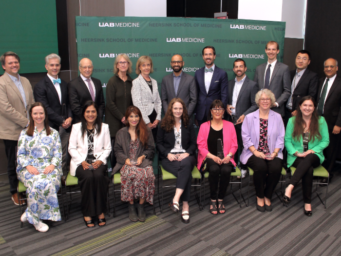 A group of people in two rows. The front row is seated, while the back row stands in front of a green backdrop.
