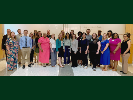 Group of 24 professionals posing together and smiling in a modern office lobby.