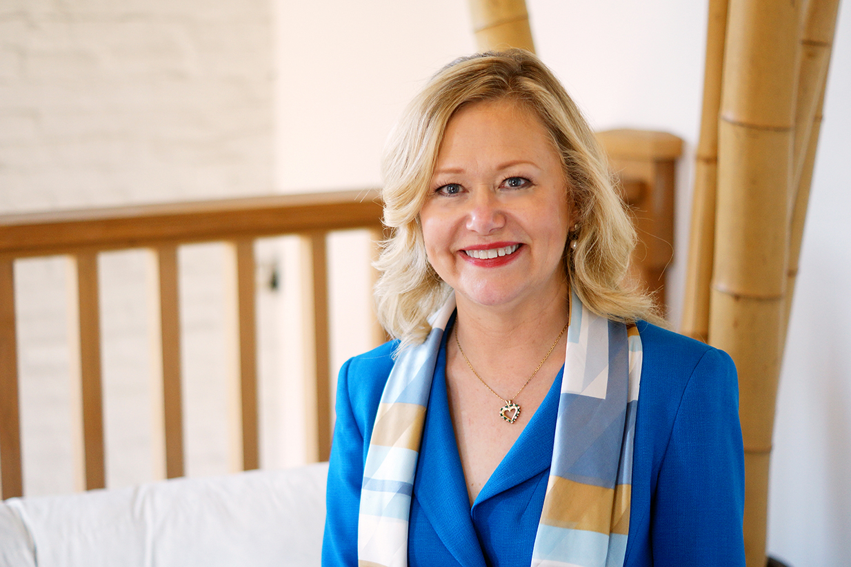 Dr Larson smiling for a headshot in a blue blazer and a yellow and blue scarf