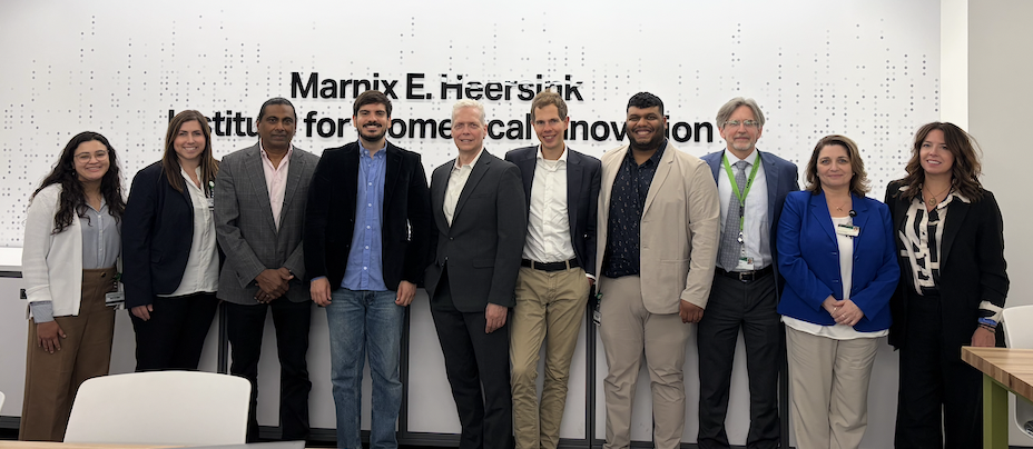 A group of 10 business professionals smiling and standing in front of a sign on the wall that reads Marnix E Heersink Institute for Biomedical Innovation
