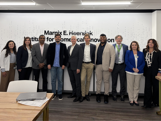 A group of 10 business professionals smiling and standing in front of a sign on the wall that reads Marnix E Heersink Institute for Biomedical Innovation