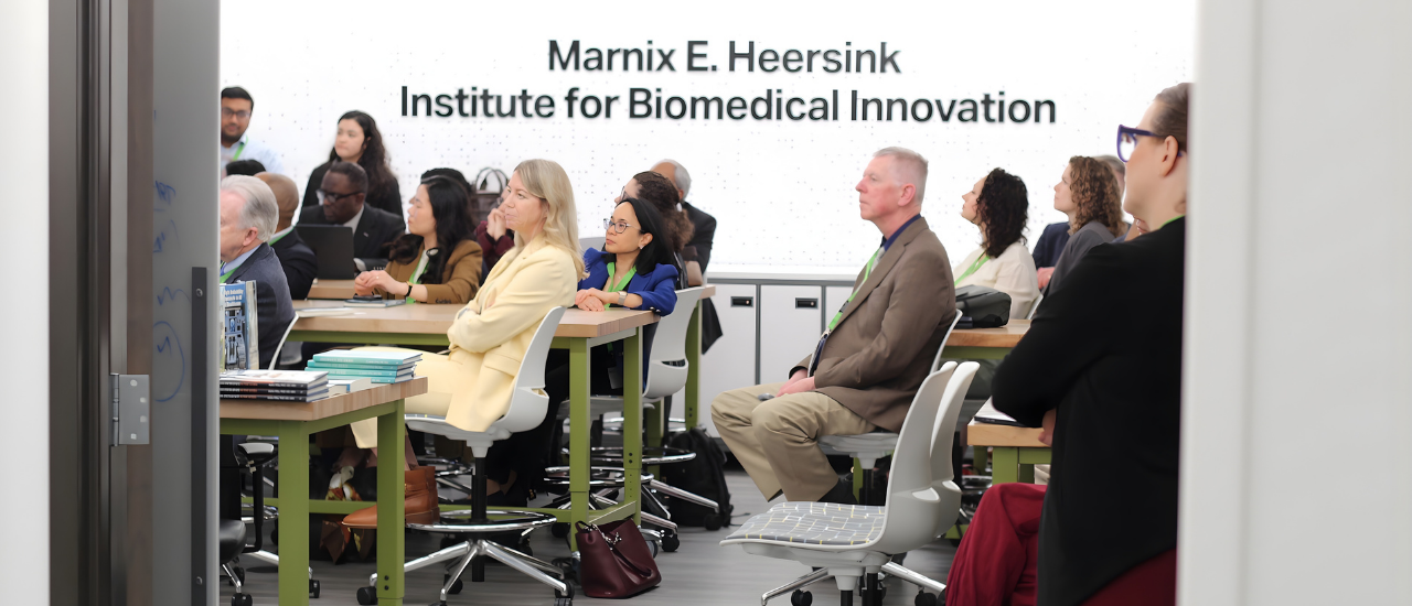 UAB/McM committee members sit and listen to lecture in the lab, in front of the Marnix E. Heersink Institute for Biomedical Innovation sign
