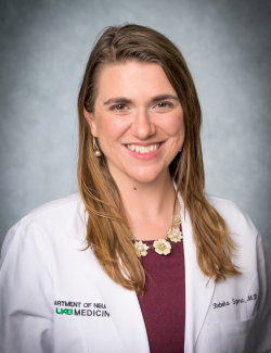 Rebeka Sipma, M.D., wearing a white medical coat and floral necklace, posed against a gray background.