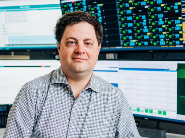 Dr. Michael Lyerly, MD (Associate Professor, Neurology) is standing in front of a large cube with a network of teleheath (telemedicine) monitors