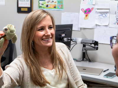 Blond ophthalmologist holds up stuffed turtle to assess eye motion of child