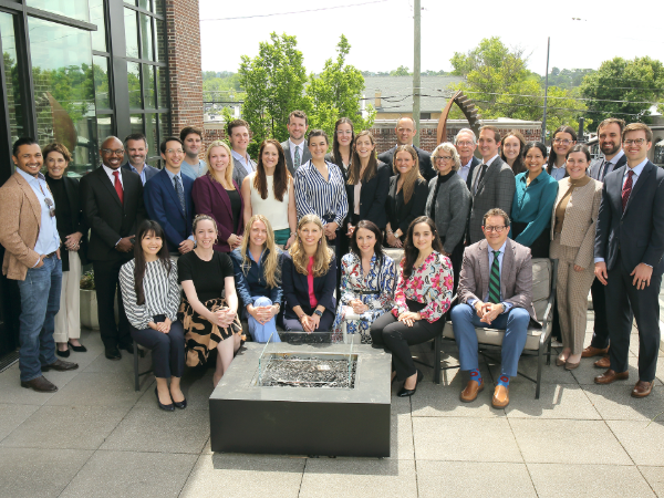 Large group in business attire posing on an outdoor terrace around a fire pit on a sunny day.