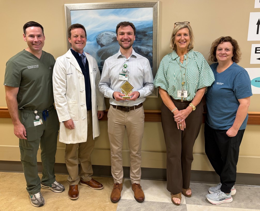 Five people standing in a hallway with champion of safety, Adam Hubler, holding a plaque