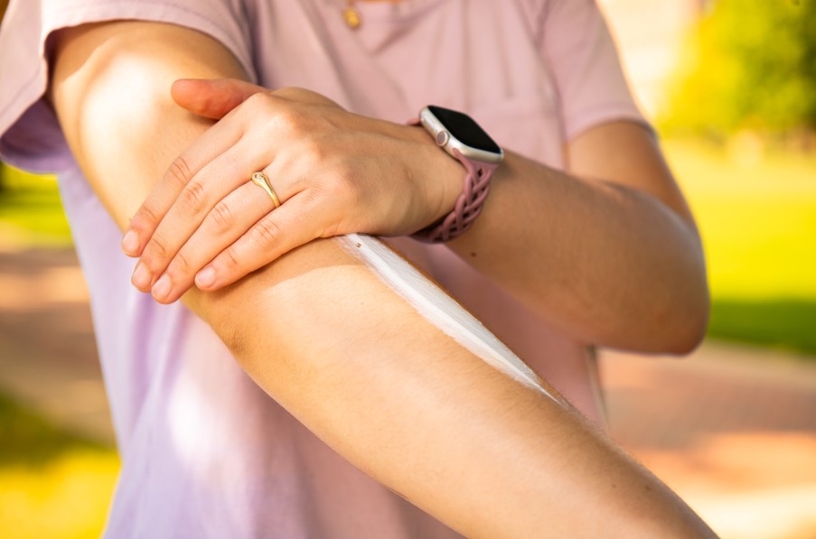 arms extended with one hand applying sunscreen on the other arm