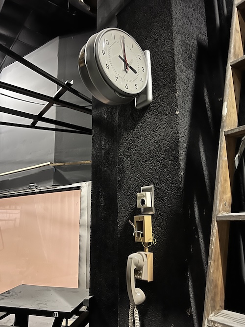 A clock fixed above a wired telephone used by projector technicians.