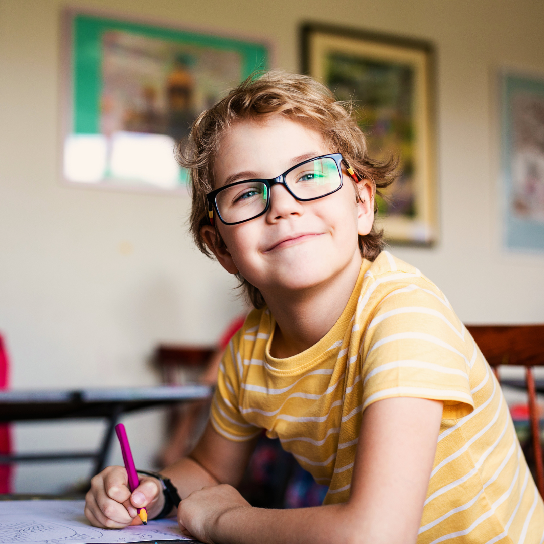 Boy wearing glasses seated at a desk in a classroom