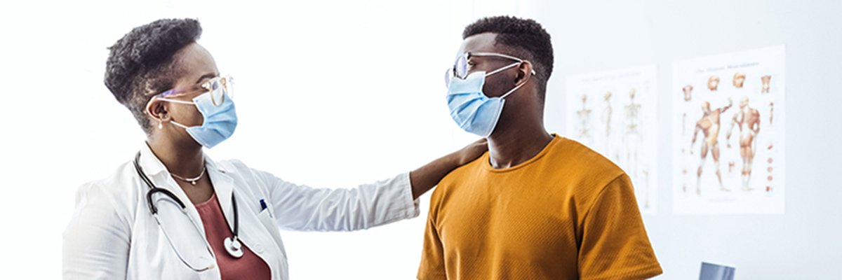 Black female doctor communicating with a patient while wearing protective face mask during medical appointment.