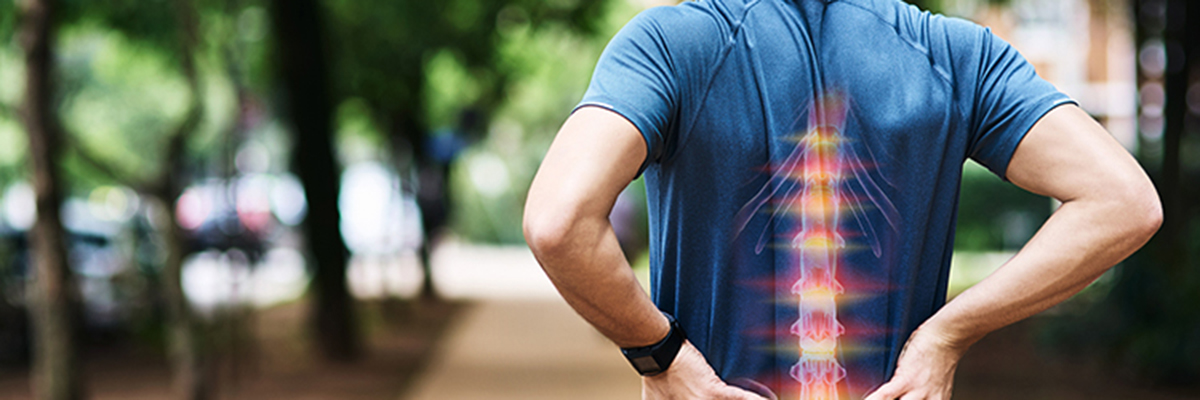 Rear view shot of a sporty young man holding his back in pain while exercising outdoors