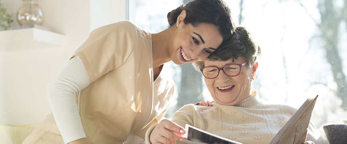 Smiling senior woman watching photobook with happy caregiver