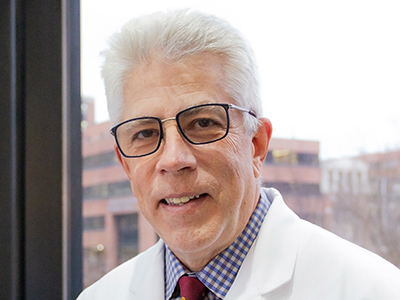 Dr. John Holcomb wearing a whitecoat with gray hair smiling for a photo