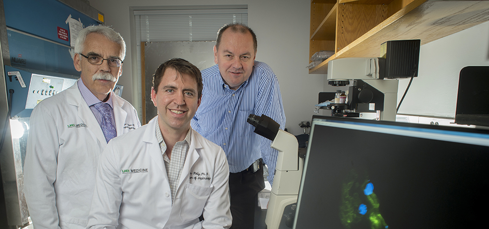 Dr. Bruce Julian, MD (Professor, Nephrology) wearing white medical coat, Dr. Colin Reily, PhD (Instructor, Nephrology) wearing white medical coat, and Dr. Jan Novak, PhD (Professor, Microbiology) sitting and standing beside computer and other equipment in laboratory, 2017