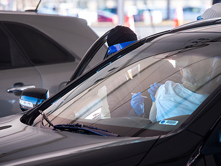 From side, a healthcare worker is wearing PPE (Personal Protective Equipment) head cover, face shield, face mask, jacket, and gloves as she vaccinates an individual sitting in vehicle as UAB and the City of Hoover open up a COVID-19 Vaccination Site at the Hoover Met Complex on February 2, 2021.   