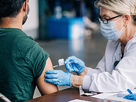 Amale student is getting vaccinated against COVID-19 by a health care worker wearing a face mask at Bartow Arena. 