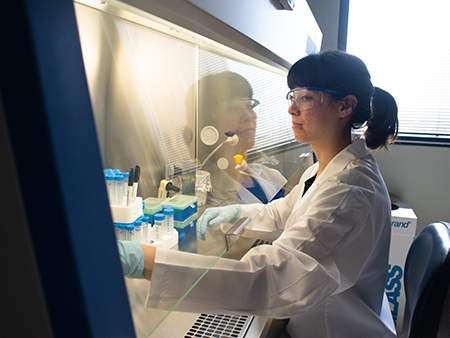 UAB Facilities Environmental Health and Safety staff member is wearing white coat and decontaminating items in a laboratory, 2019.