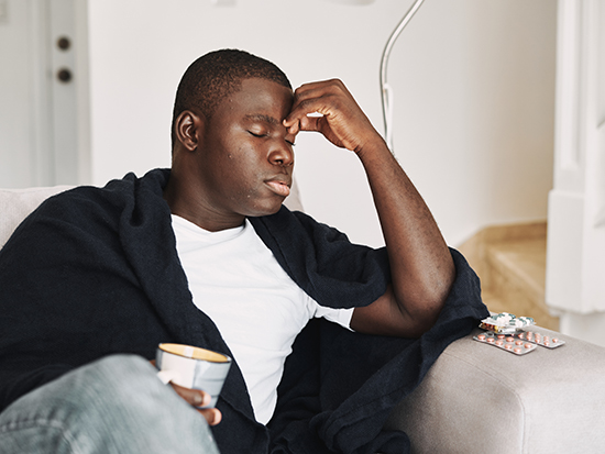 Sick man on couch holding cup of tea.