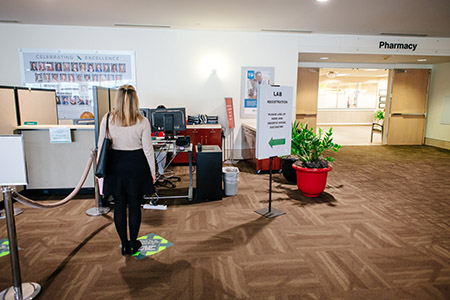 Back, a female patient is standing on a social distancing marker in front of a registration desk at a medical office in the Kirklin Clinic during COVID-19 (Coronavirus Disease), May 2020.