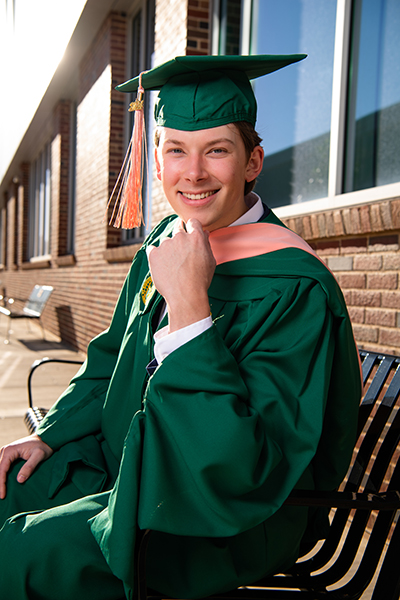 David Russell sitting on bench in graduation regalia. 