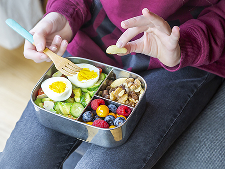 salad with avocado, cucumber, tomatoes, parmesan and eggs in a lunch box, trail mix and berries