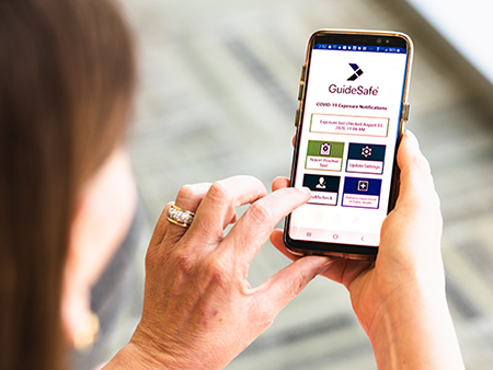 Close-up of mobile phone displaying a screen from the GuideSafe Exposure Notification app being held by unidentified woman; users of the app can anonymously share a positive COVID-19 test result - and be anonymously notified of potential previous close contact with someone who later reports a positive COVID-19 test result - without sharing anyone's identity; August 2020.