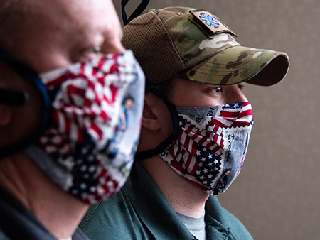 From side, father and son, William "Bill" Mayfield (Emergency Preparedness Manager, UAB Healthcare System) and Matthew Mayfield (Student, Public Health) are wearing homemade medical masks (made with material representing the 9/11 attacks) around their necks while standing in the UAB Hospital COVID-19 (Novel Coronavirus) Command Center, North Pavilion, April 2020.