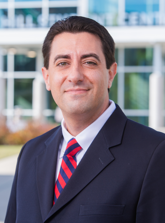 Matthew Macaluso standing outside the Hill Student Center wearing a navy coat and a red and blue stripped tie. 