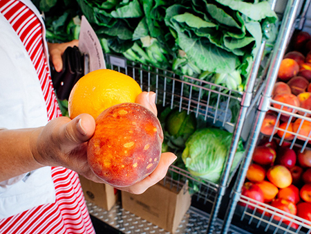 Hand holding a peach and an orange. 