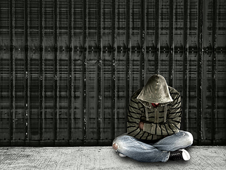 Homeless man wearing jeans and hooded top sitting on ground