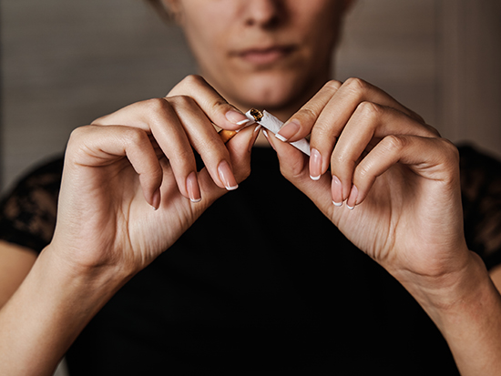 Unrecognizable young woman breaking a cigarette in half to stop smoking. Concept of smoking and addiction.