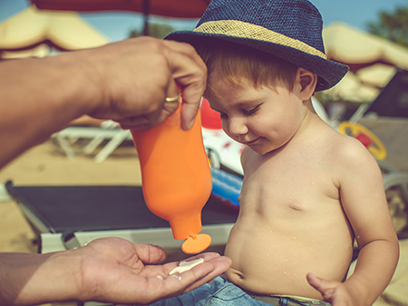 Father applying sun protection lotion with his child near the sea in hot summer