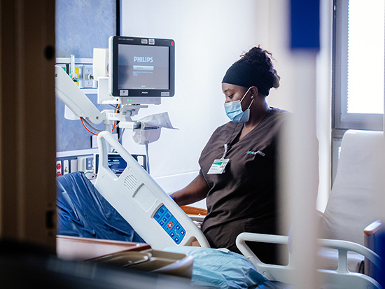 Kareshar Payne (Environmental Services Specialist - Hospital, Environmental Services) is wearing a PPE (Personal Protective Equipment) face mask and using disinfecting and cleaning wipes on bed rails while performing a post-discharge "terminal cleaning" of an inpatient hospital room during the COVID-19 (Coronavirus Disease) pandemic, May 2020.