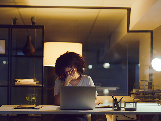 Shot of a young businesswoman looking stressed while using a laptop during a late night at work