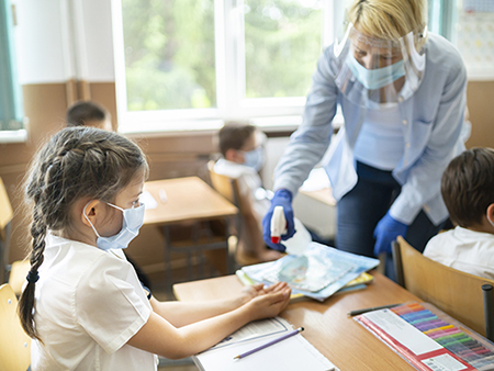 Service staff disinfecting hands of a girl in the classroom