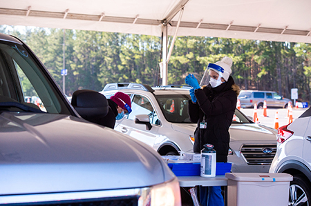 From side, a black female healthcare worker is wearing PPE (Personal Protective Equipment) face mask and gloves as she vaccinates a black male at the UAB COVID-19 Vaccination Site at Parker High School on February 10, 2021/.