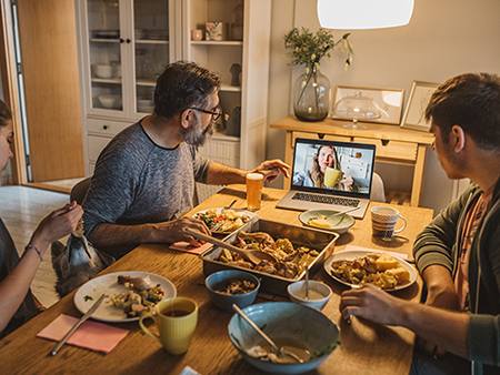 Family have diner during isolation period. Mother is not with them, they talking with her on laptop