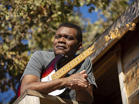 Outdoor photo of Robert Cray with a guitar. 