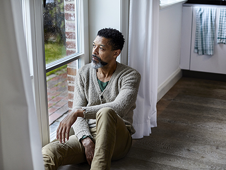 Man with depression looking outside the window on a rainy day. 