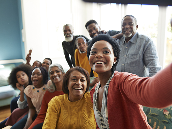 Smiling young woman taking selfie with family and friends celebrating Christmas festival at home