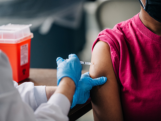 A Black female is getting vaccinated against COVID-19 (Coronavirus Disease) by a health care worker. 