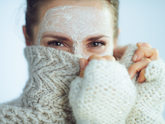 Women in skincare face mask covers mouth and nose with sweater.