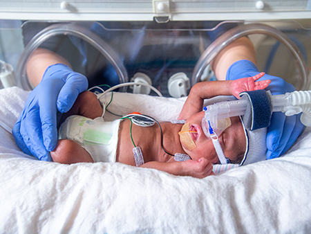 Close-up, nurse's hands wearing blue safety gloves are tending to a premature baby in a neonatal incubator in the Regional Neonatal Intensive Care Unit (NICU), 2019.